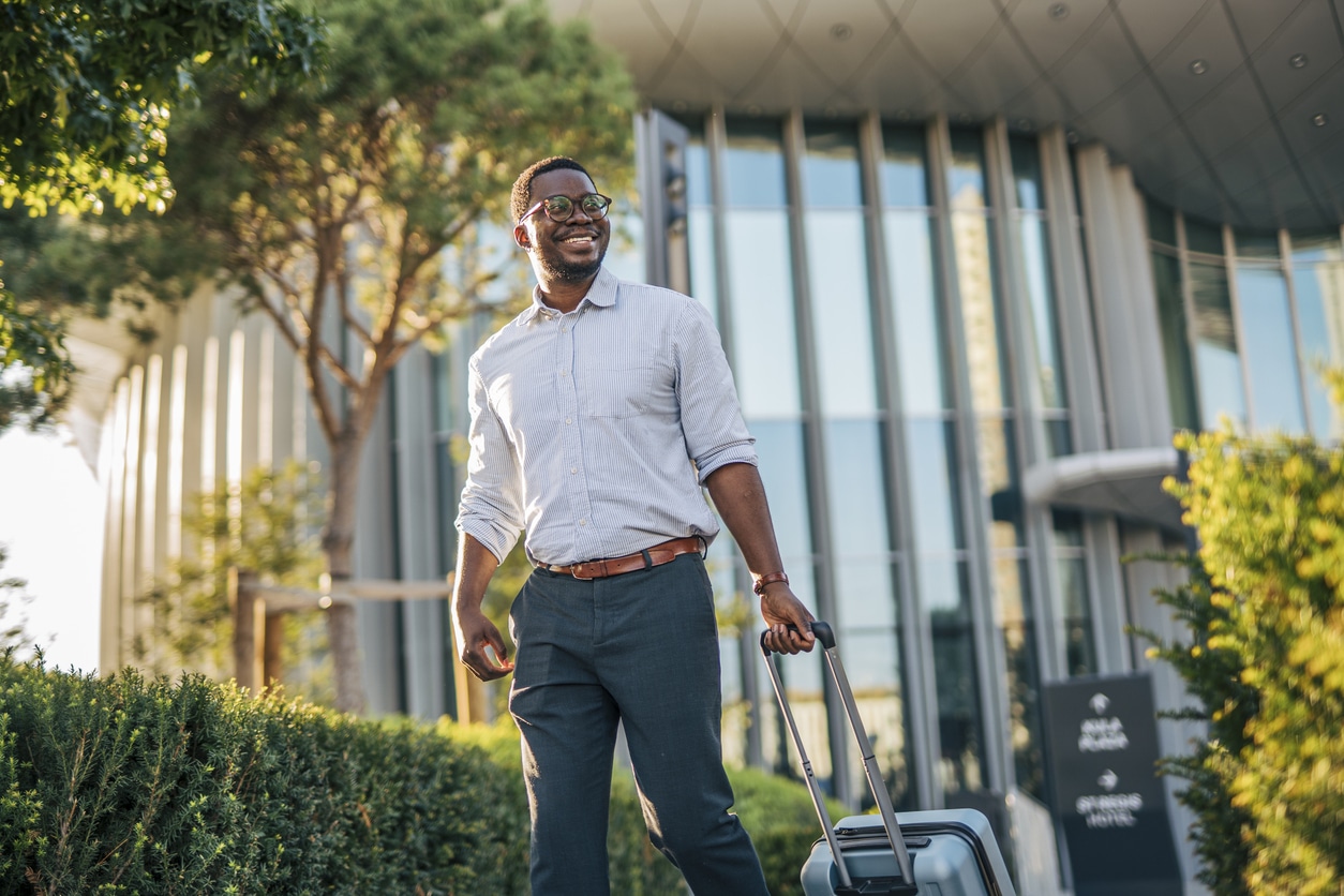 Smiling professional man with luggage outside modern office building, representing expats negotiating relocation and assignment packages