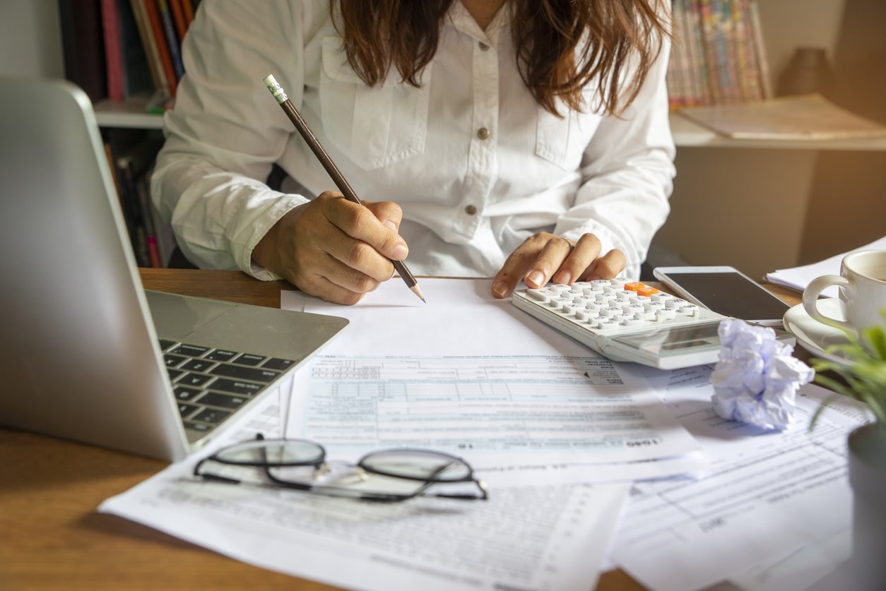 Person working at a desk with tax forms, calculator, and laptop, representing international tax filing deadlines by country.